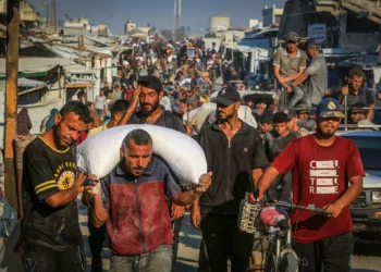 Gazatíes caminan por las calles con sacos de harina después de que los camiones de ayuda humanitaria llegaran a través del cruce de Kerem Shalom controlado por Israel hacia el sur de Gaza, en Jan Yunis, el 24 de julio de 2025. (Abed Rahim Khatib/Flash90)